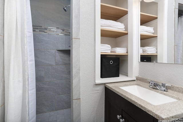 bathroom with a textured wall, tiled shower, and vanity