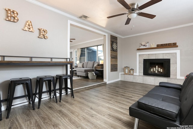 living area featuring visible vents, a tiled fireplace, ornamental molding, and wood finished floors