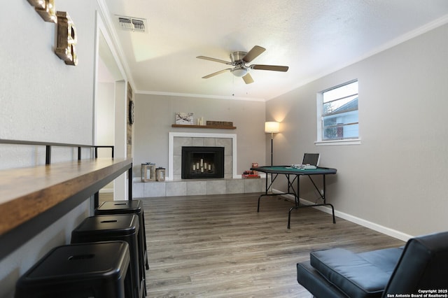 interior space with a fireplace, crown molding, visible vents, a ceiling fan, and wood finished floors