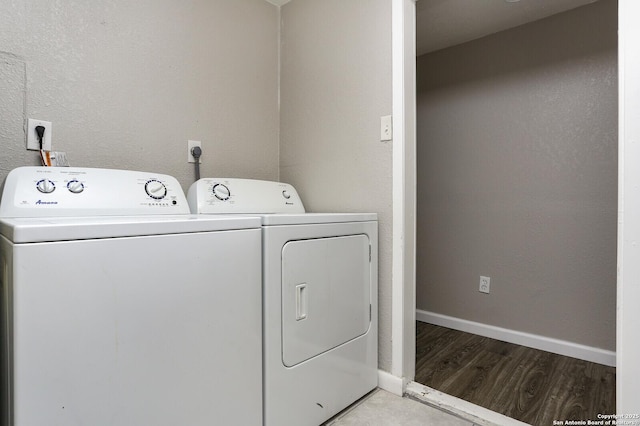 clothes washing area featuring laundry area, baseboards, a textured wall, wood finished floors, and separate washer and dryer