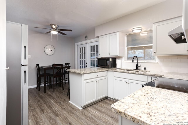 kitchen with light wood-style flooring, freestanding refrigerator, a peninsula, black microwave, and a sink