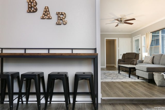 interior space with baseboards, ceiling fan, dark wood-type flooring, crown molding, and a kitchen bar