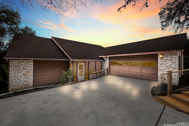 view of front facade with stone siding, a shingled roof, and concrete driveway