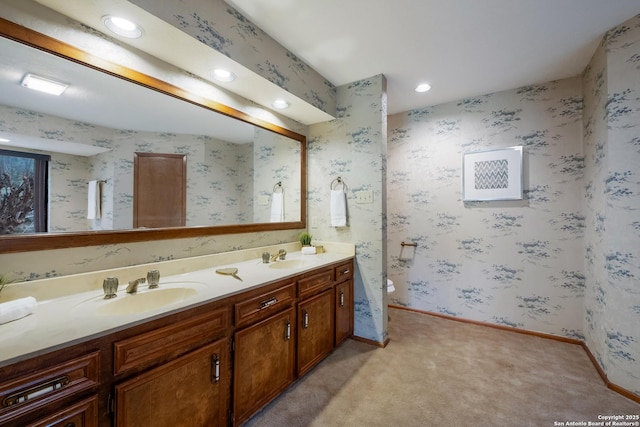 bathroom with double vanity, wallpapered walls, baseboards, a sink, and recessed lighting