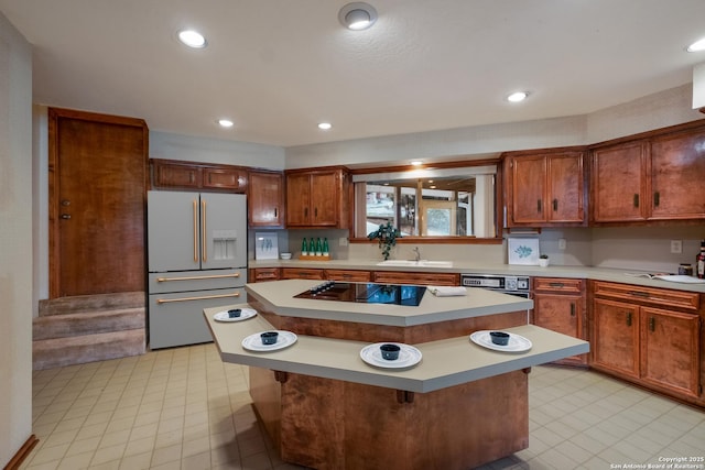 kitchen featuring high end fridge, light countertops, a kitchen island, a sink, and black electric cooktop