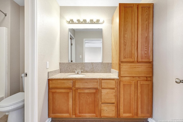 full bathroom with toilet, a textured wall, and vanity