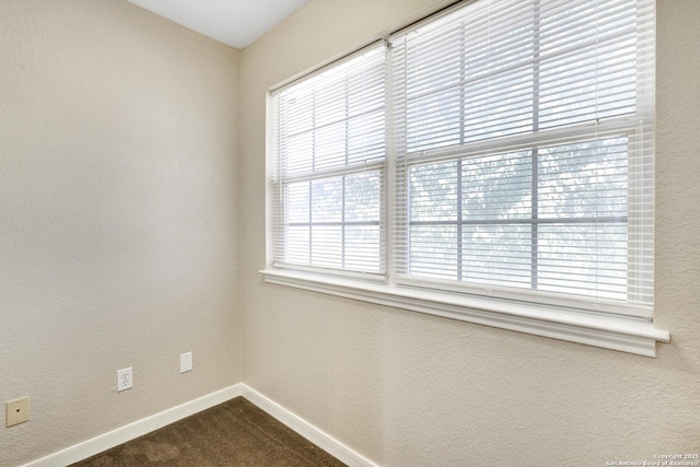 empty room with dark carpet, a textured wall, and baseboards