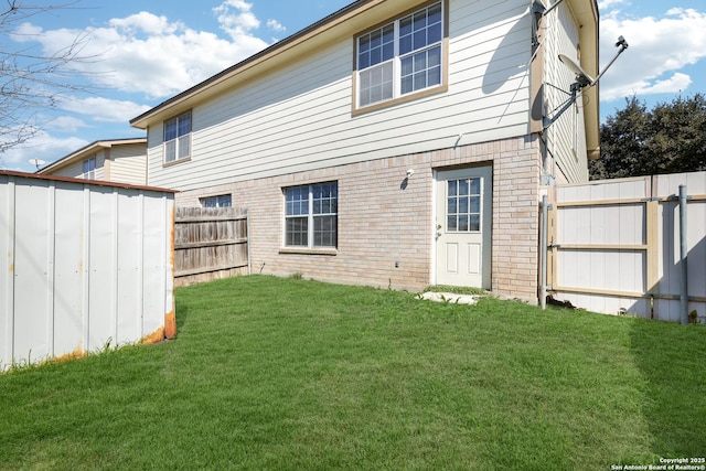 back of house featuring a yard, a fenced backyard, and brick siding