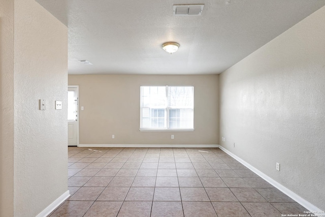 unfurnished room featuring light tile patterned floors, baseboards, visible vents, a textured wall, and a textured ceiling