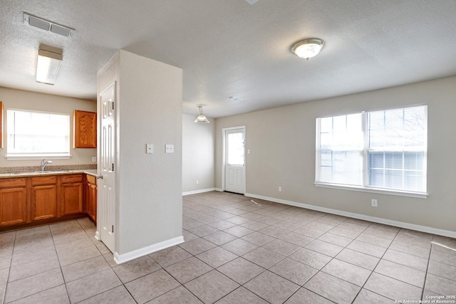 kitchen with brown cabinetry, light tile patterned flooring, a sink, and visible vents