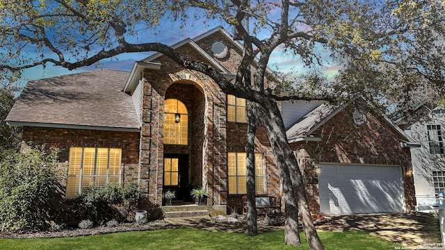 traditional-style home with roof with shingles, brick siding, driveway, and an attached garage