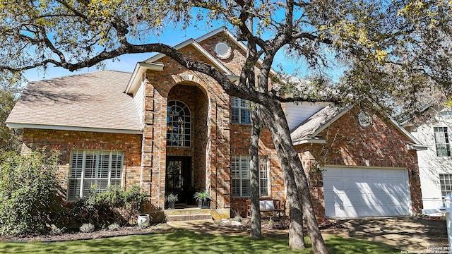 traditional-style house with brick siding, a shingled roof, an attached garage, driveway, and a front lawn