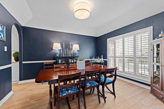 dining space with light wood-style flooring, arched walkways, and baseboards