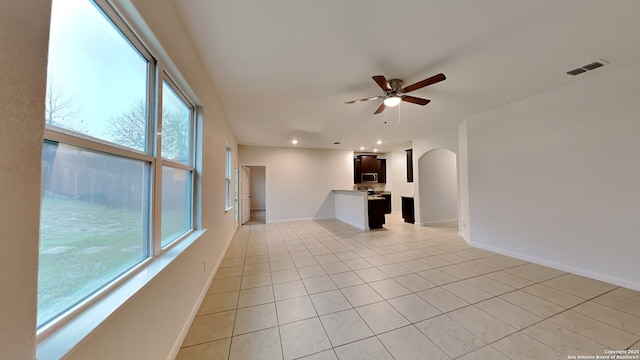 unfurnished living room featuring arched walkways, a wealth of natural light, visible vents, and baseboards