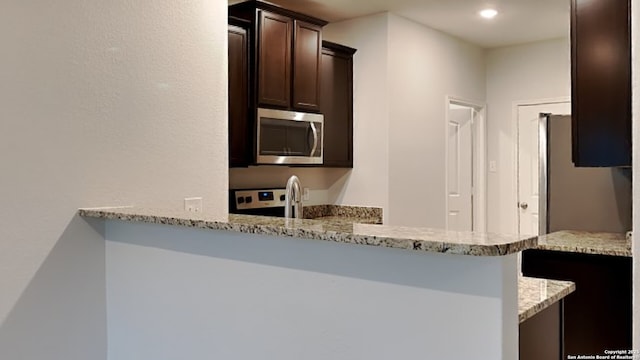 kitchen with range, stainless steel microwave, light stone countertops, dark brown cabinets, and a sink