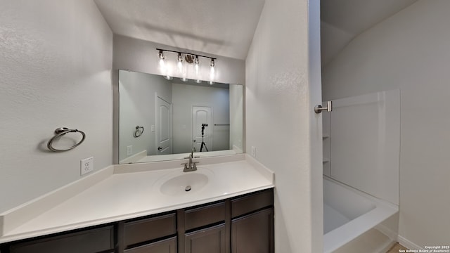 full bath featuring a textured wall, vanity, and a bathing tub