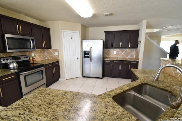 kitchen with stone countertops, stainless steel appliances, a sink, visible vents, and decorative backsplash