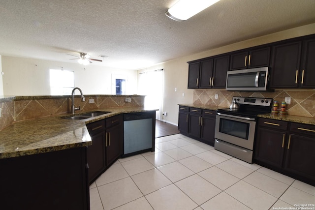 kitchen with light tile patterned floors, stainless steel appliances, tasteful backsplash, a sink, and dark stone countertops