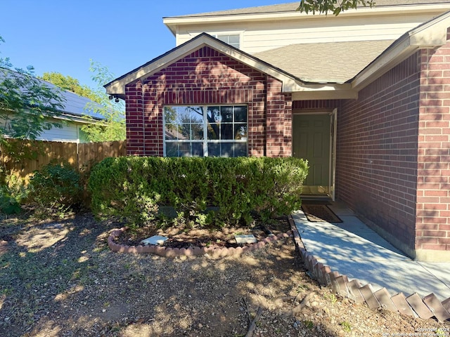 entrance to property featuring a shingled roof, brick siding, and fence