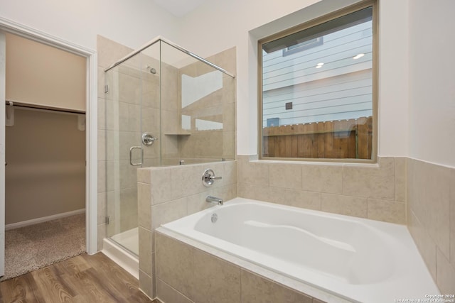 full bathroom with a shower stall, a spacious closet, a bath, and wood finished floors