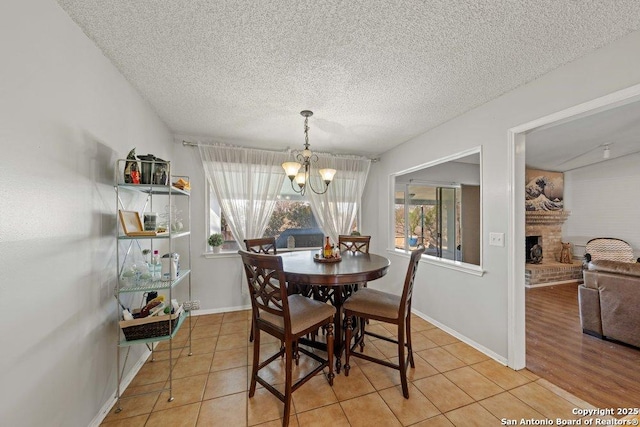 dining space featuring a chandelier, a brick fireplace, a textured ceiling, and light tile patterned floors