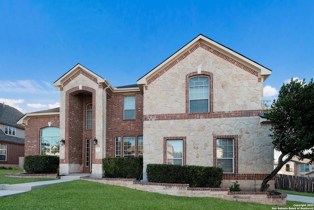 view of front of home featuring stone siding, a front yard, fence, and brick siding