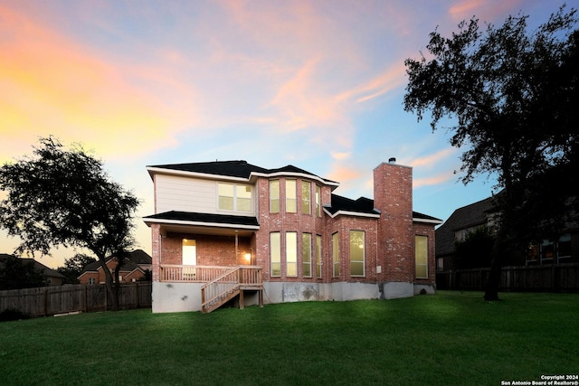 back of property featuring brick siding, a yard, a chimney, and fence