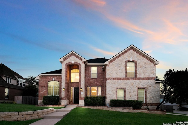 view of front of house with stone siding, brick siding, a yard, and fence