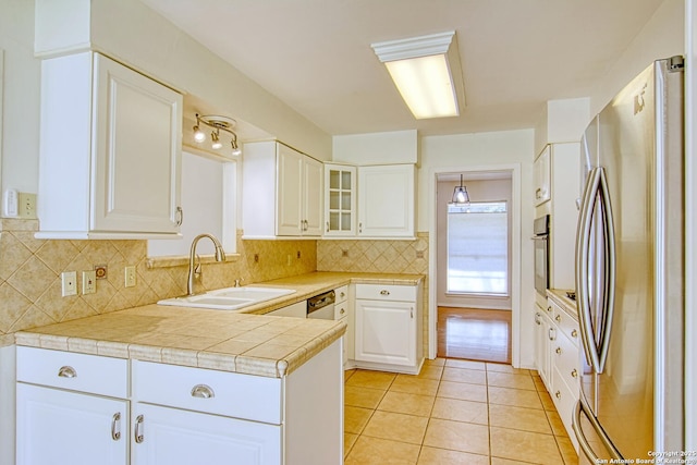 kitchen featuring wall oven, freestanding refrigerator, light tile patterned flooring, a sink, and white cabinetry