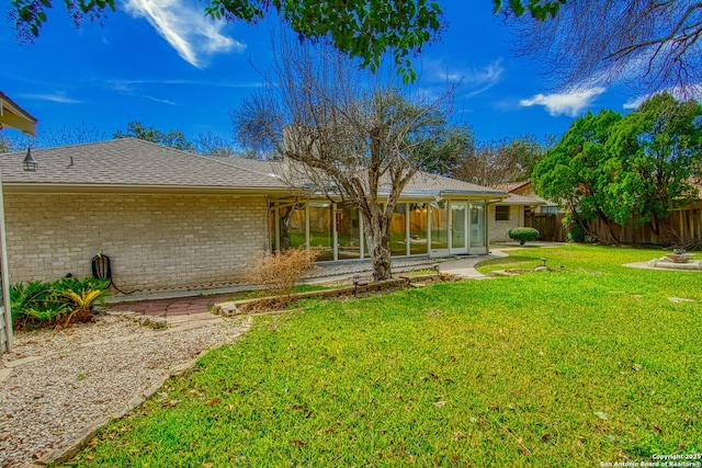 rear view of property with brick siding, a shingled roof, fence, a sunroom, and a yard