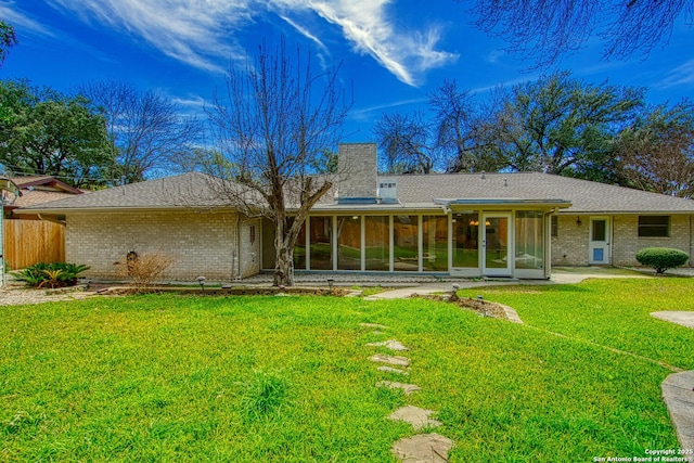 rear view of house with brick siding, a lawn, a chimney, and a sunroom