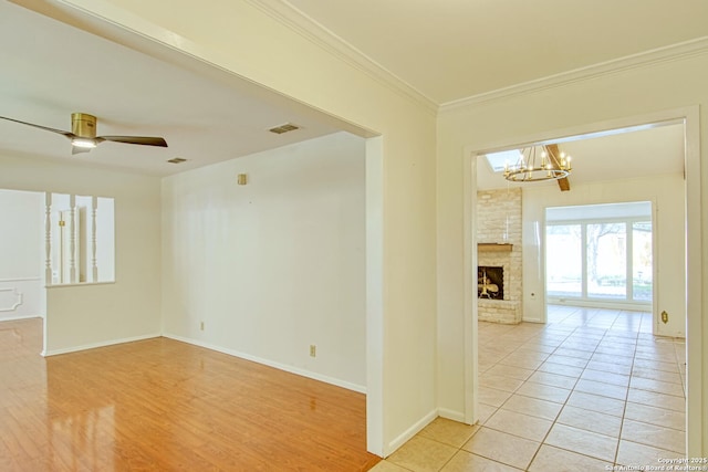 spare room with a fireplace, visible vents, ornamental molding, baseboards, and ceiling fan with notable chandelier