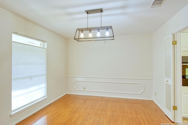 unfurnished dining area with light wood-style floors, visible vents, and wainscoting