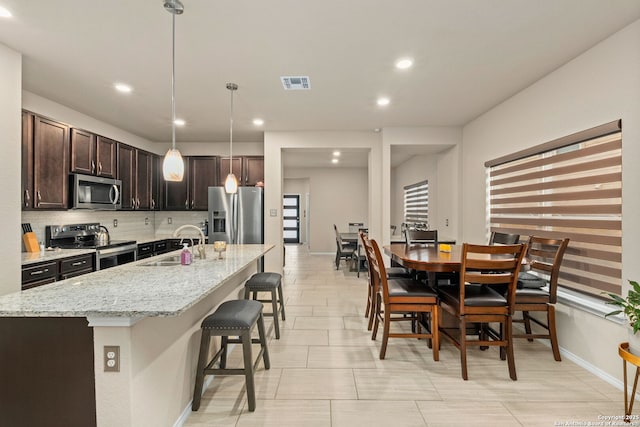 kitchen featuring visible vents, appliances with stainless steel finishes, a sink, dark brown cabinets, and backsplash