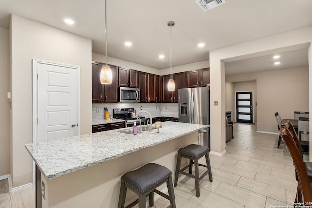 kitchen with visible vents, appliances with stainless steel finishes, a sink, dark brown cabinets, and backsplash