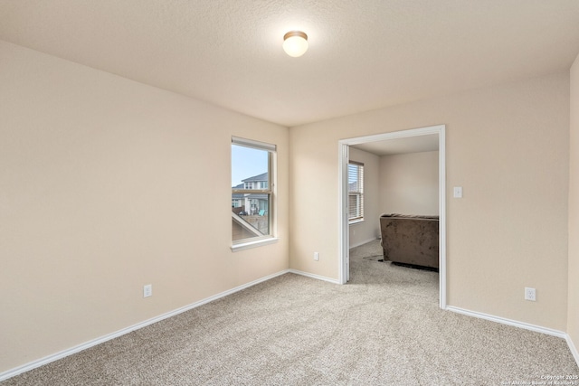 empty room with light carpet, a textured ceiling, and baseboards