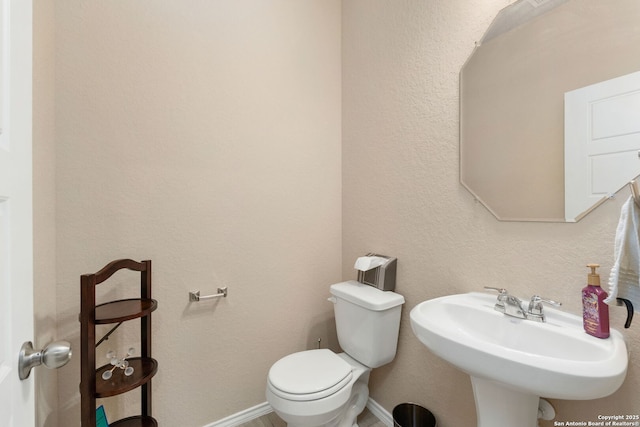 half bathroom featuring baseboards, a sink, and toilet