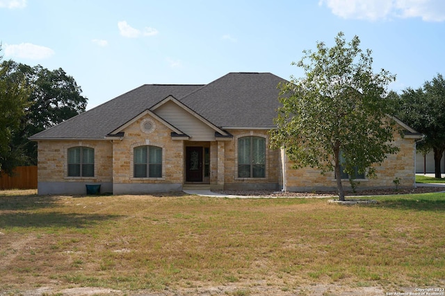 view of front of house with stone siding, a shingled roof, and a front yard