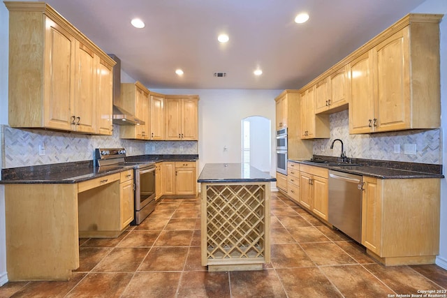 kitchen with arched walkways, stainless steel appliances, visible vents, a sink, and wall chimney range hood