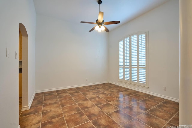 empty room featuring arched walkways, lofted ceiling, a ceiling fan, and baseboards