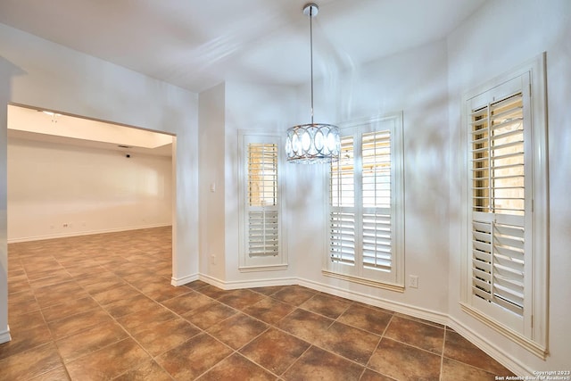 unfurnished dining area featuring dark tile patterned floors, baseboards, and a chandelier