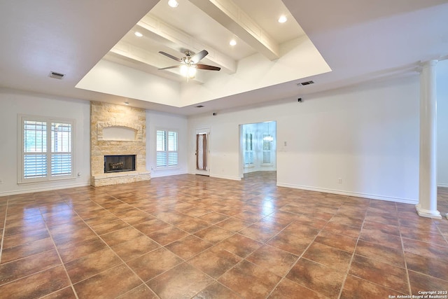 unfurnished living room with ceiling fan, a stone fireplace, visible vents, baseboards, and beam ceiling