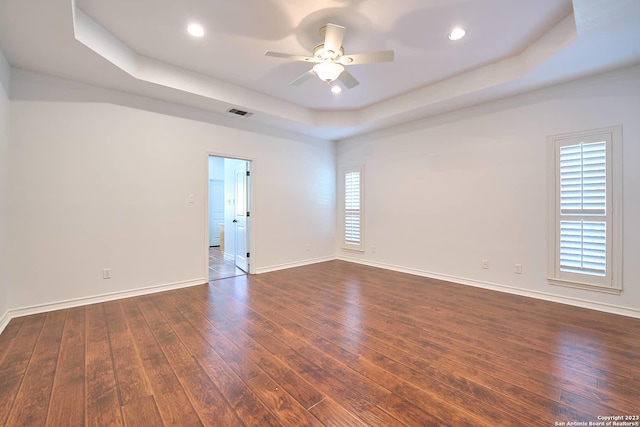 empty room with visible vents, baseboards, a raised ceiling, ceiling fan, and dark wood-style flooring