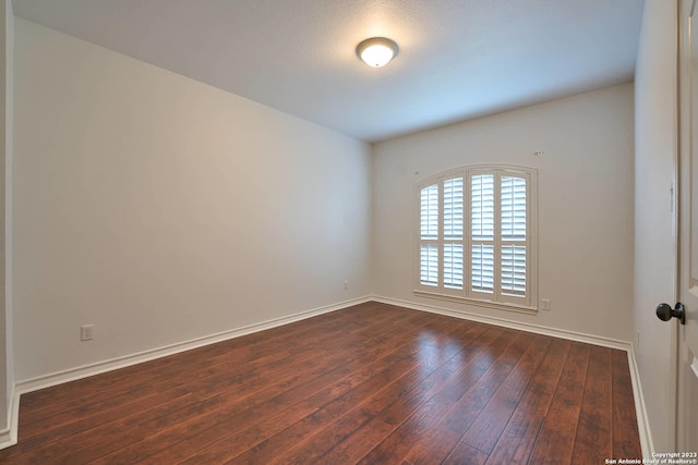 spare room with dark wood-style flooring and baseboards