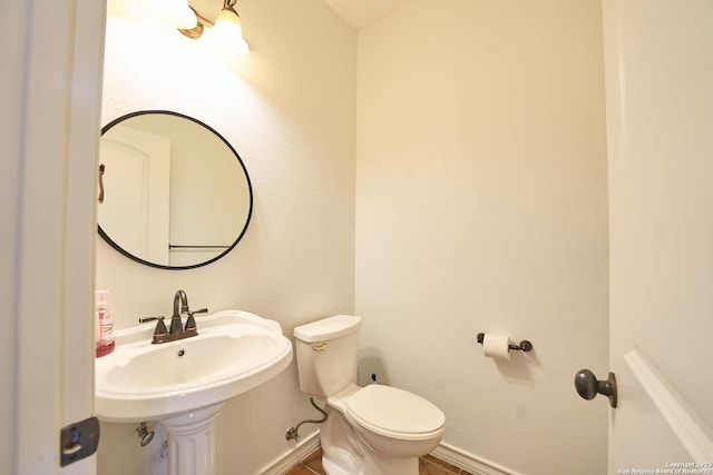 bathroom featuring toilet, baseboards, and a sink