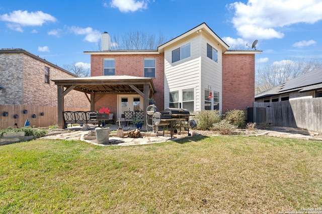 rear view of house featuring brick siding, a chimney, a lawn, a gazebo, and fence