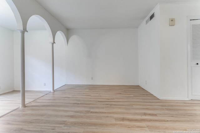 unfurnished room with light wood finished floors, visible vents, and arched walkways