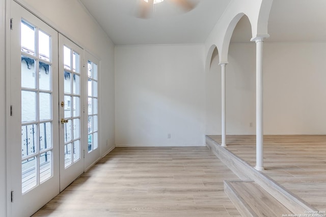 unfurnished room with arched walkways, ceiling fan, french doors, light wood-type flooring, and ornate columns