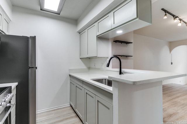 kitchen with stainless steel appliances, light wood-type flooring, light countertops, and a sink