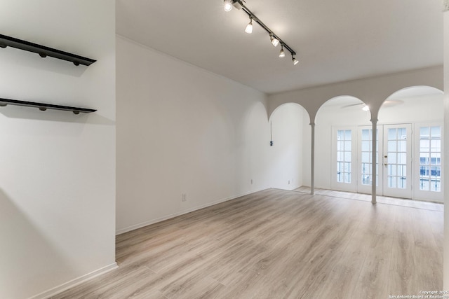 empty room featuring arched walkways, baseboards, rail lighting, and light wood-style floors